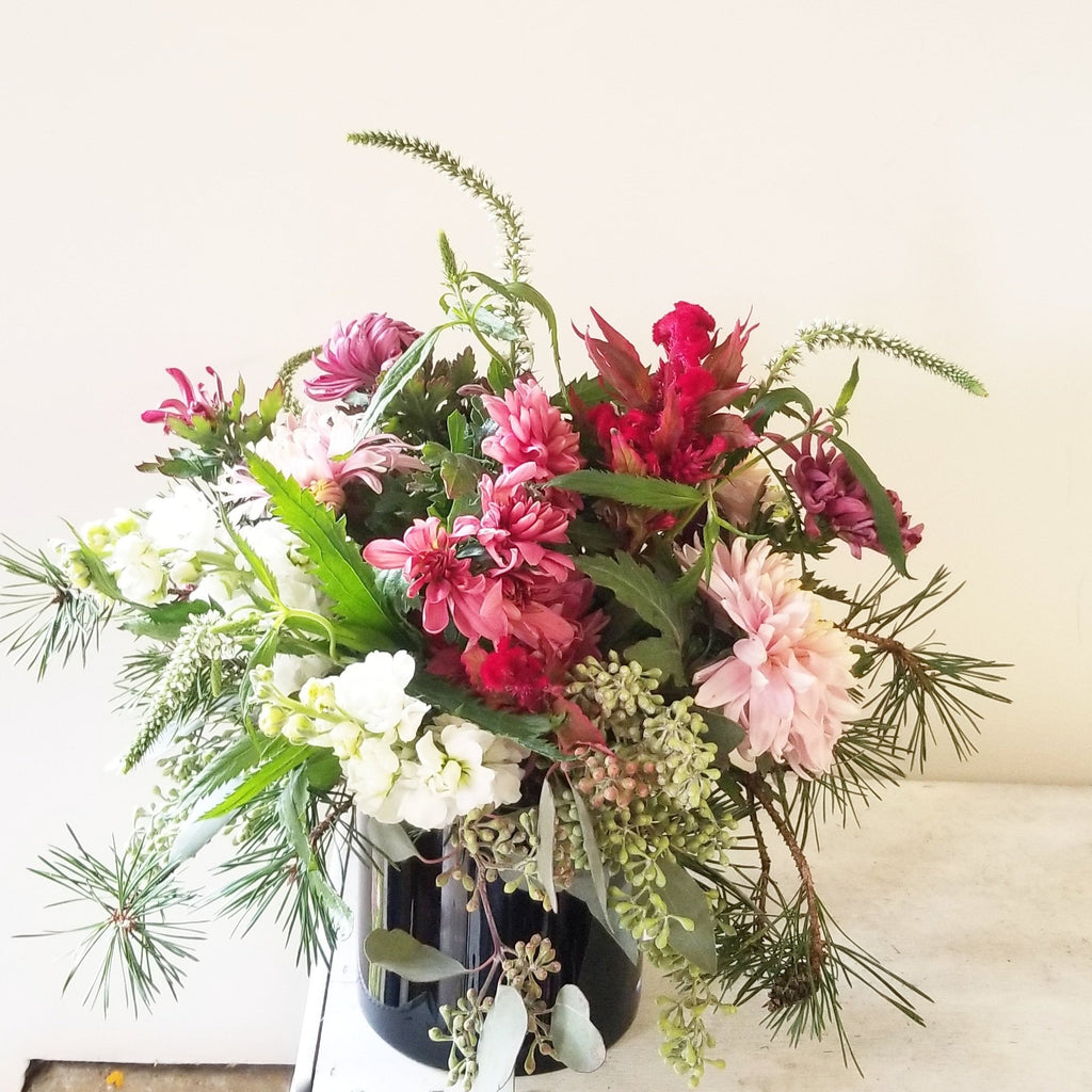 Pacific Northwest inspired pink flowers with evergreens in dark glass vase