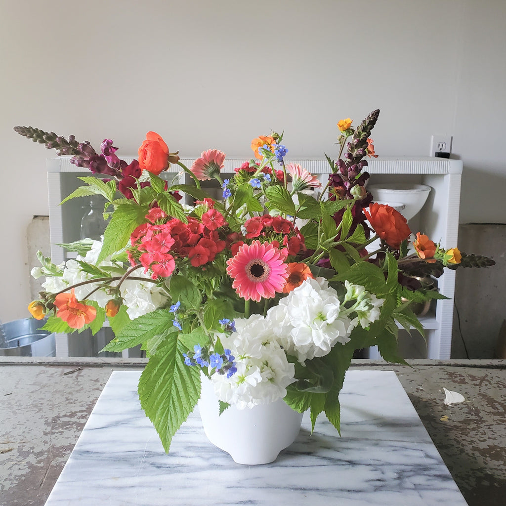 bright mixture of seasonal flowers and greenery in white ceramic vase